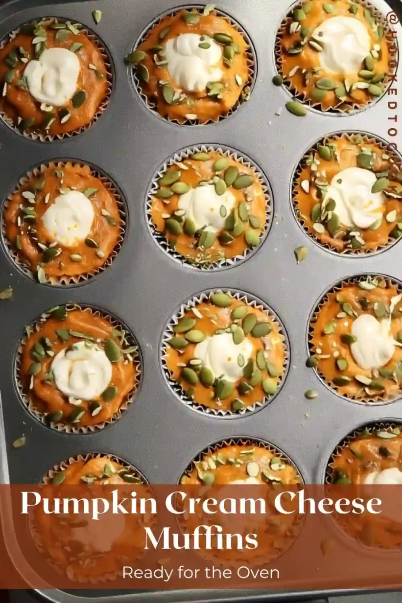pumpkin cream cheese muffins in a muffin tin with cream cheese swirl and pepitas