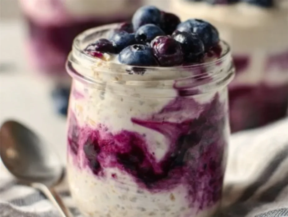 Blueberry cheesecake overnight oats in a glass topped with fresh blueberries