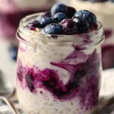 Blueberry cheesecake overnight oats in a glass topped with fresh blueberries