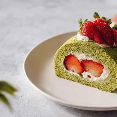 Delicious Strawberry Matcha Roll Cake topped with fresh strawberries and matcha powder.